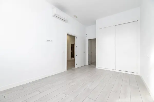 An empty room with built-in wardrobes with white sliding doors, access to an en-suite bathroom and air conditioning units hanging high on the wall