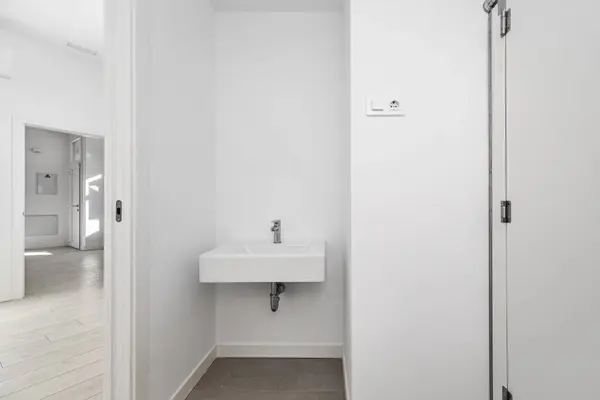 A bathroom with white porcelain sink, white pressed wood screen and gray tiles