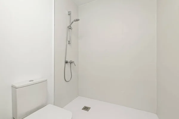 A bathroom with a shower cabin with white walls without a screen next to a toilet