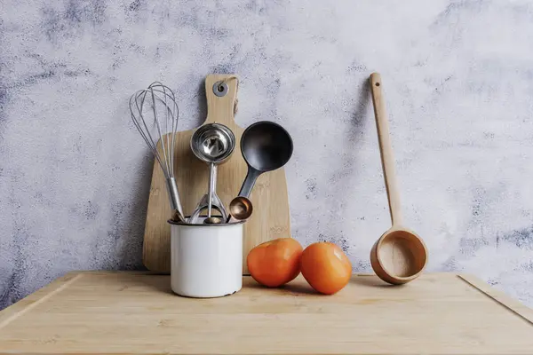 Wooden and metal kitchen utensils along with two tomatoes on a bamboo wooden board