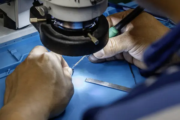 Image of a repair technician in an electronics store working at his station with an electron microscope soldering some small parts