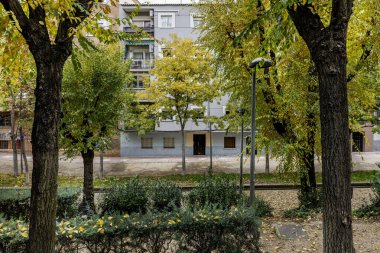 Çalılıklarda bir sürü ağaç ve sokak lambası olan parkın yanındaki bir apartmanda.