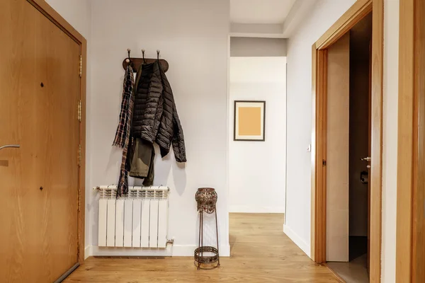 Hallway of a home with armored access door, an aluminum radiator, wooden floors and a coat rack with hanging clothes