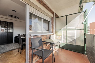 İçinde masa ve sandalyeler olan küçük bir teras. Mobilyalı bir oturma odasının girişi ve perdesi.