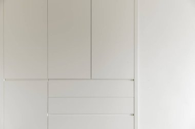 İçinde çekmeceler, beyaz ahşap kapılar ve beyaza boyanmış duvarlar olan bir yatak odası.