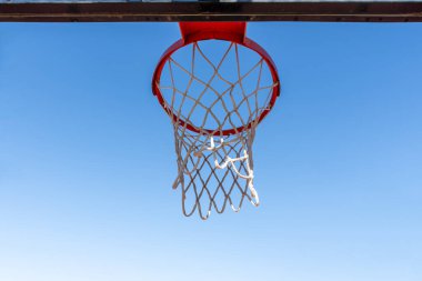 Mavi gökyüzüne karşı tipik turuncu renkli metal bir basketbol sepeti.