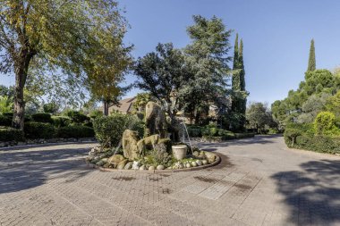 Tek bir ailenin yaşadığı geniş bir arazide, kaldırımlı bir yürüyüşün çardağında bir çeşme.