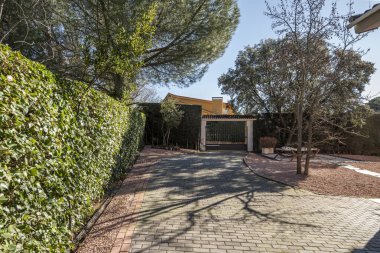 Erişim, çevresi kırmızımsı çakıl ve çitlerle kaplı bir evin arsası içinde bir garaja doğru yürür.