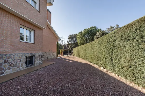 Kırmızımsı çakıl ve barakanın yanındaki ağaçlarla kaplı bir evin arsası.