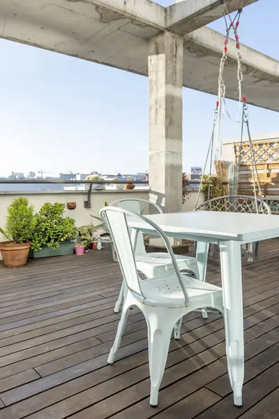 Bitkilerle dolu bir şehir terası ve uyumlu sandalyeli metal bir masa.