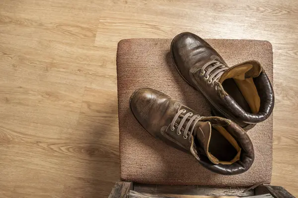 A pair of brown leather boots with triple stitching on an old seat seen from above in a room with brown parquet floors