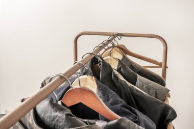 Beyaz bir odada kamuflaj izleri olan farklı kumaşlarla erkek giysileri taşıyan ahşap askılarla dolu krem rengi metal çubuklar.