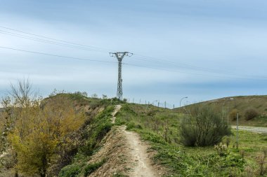 Dar bir dağ bisikleti, yüksek voltaj pilonuna doğru küçük bir yokuş yukarı gidiyor.