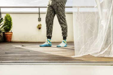 Tahta bir zeminle terasta yürüyen ve taklit izi olan elastik pantolon giyen bir adamın bacakları.