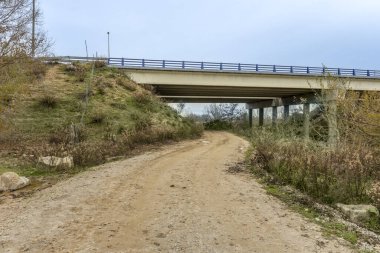 Otoyol köprüsünün altından geçen toprak bir yol. Dairesel beton sütunlu iki bağımsız at arabası var.