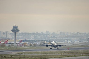 Kontrol kulesinin yanındaki havaalanından inerken iki jet motoru olan tamamen beyaz bir yolcu uçağı.