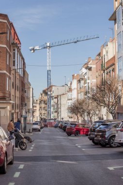 Park etmiş araçları olan bir şehir caddesi ve arka planda büyük bir inşaat vinci.