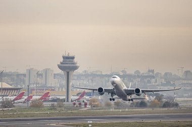 Gün batımında kontrol kulesinin yanındaki havaalanından yükselen iki jet motorlu tamamen beyaz yolcu uçağı.