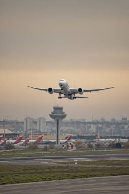 Hava alanından gün batımında kızıl gökyüzünde yükselen iki jet motorlu tamamen beyaz bir yolcu uçağı.