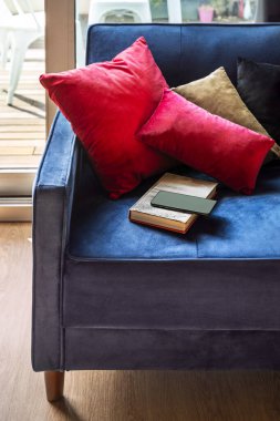 Kağıt kaplı güzel mavi kadife bir kanepe, akıllı bir telefon ve parlak ahşap döşemeli bir odada renkli yastıklar.