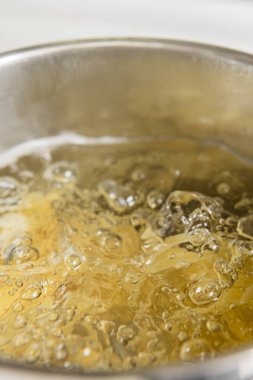 Ev mutfağında suyla dolu paslanmaz çelik bir tencerede pişen buğday eriştesi.