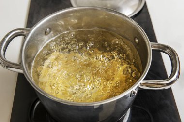 Buğday eriştesi paslanmaz çelik bir tencerede pişirildi. İçi kaynar suyla dolu, siyah seramik bir kafeteryada.