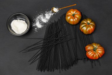 Some delicious raf tomatoes on black spaghetti and a bowl of grated cheese clipart
