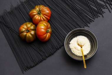 A trio of succulent ripe Raf tomatoes on a mound of black pasta next to a bowl full of grated cheese with a golden spoon clipart