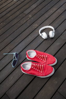 Kırmızı kulaklıklı ve güneş gözlüklü spor ayakkabılar. Çatı katı terasında kahverengi bir tahta yüzeyde.