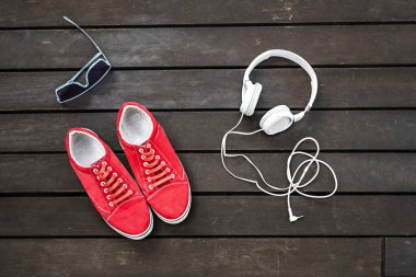 Kahverengi bir tahta yüzeyde kulaklık ve güneş gözlüğü takan kırmızı spor ayakkabılar.