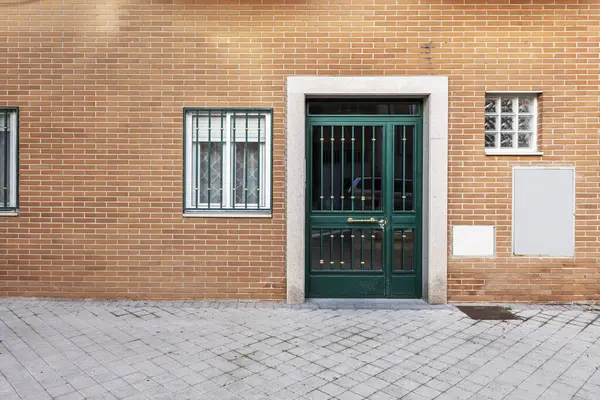 Access door on the facade of a building with a house on the ground floor with green bars on the windows