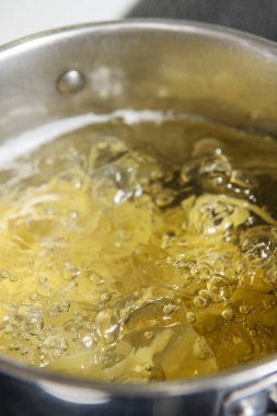 Siyah seramikte makarna pişirmek için kaynar suyla dolu paslanmaz çelik bir kap.