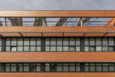 Ofis binasının ön cephesinde siyah metal pencerelerle birleştirilmiş açık kahverengi tuğladan bir duvar var.