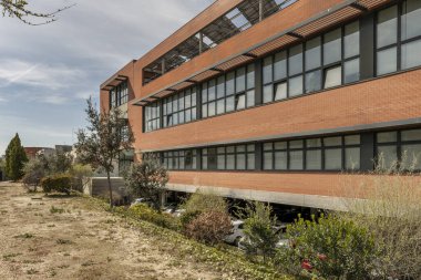 Açık kahverengi tuğla duvarlı ofis binası ve zemin katta park yeri olan siyah metal pencereler.