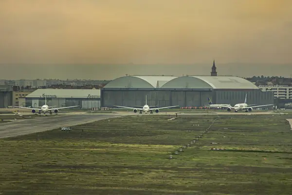 A row of passenger planes near the hangars of an airport waiting their turn to race down the runway and take off