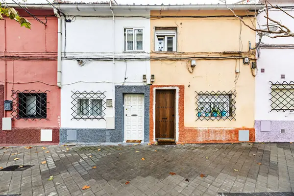 Facades of old houses of various colors of two heights with access doors to the street of different materials with metal bars on the windows