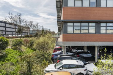 Kahverengi tuğla ve siyah metal ofis binasının ön cephesinde zemin katı açık otoparka ayrılmış.