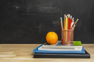 İçinde kauçuk uçlu kalemler ve turuncu renkli bakır bir sepet olan kitaplar ve defterler.