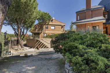 Kumlu yolları olan bir ev, karakteristik siyah döşeme kiremit çatılı bir dağ evi, çalılar ve bol ağaçlı.