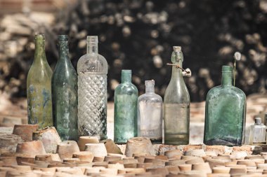 Terracotta tencerelerinin yanına istiflenmiş antika cam şişeler. 