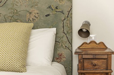 Döşemesi baskılı kumaş ve eski ahşap komodiniyle döşenmiş yatak odasının detayları.