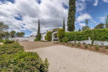 Beyaz cepheli bir çiftlik evinin ön cephesi. Duvarlarında bir sürü bitki örtüsü ve dar selvi var..