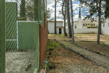 The Andalusian-style farmhouse with a small pine forest and paths marked with stones next to a fenced tennis court clipart