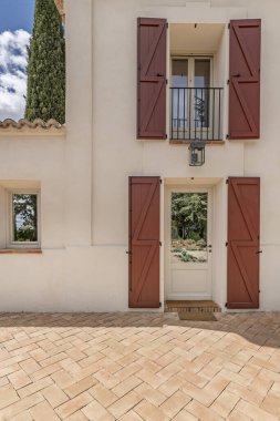 Balkonlarında kırmızı ahşap panjurlar olan beyaz bir kır evi cephesi.