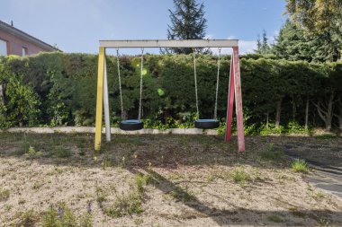 Çitleri olan çitler ve tekerlekleri koltuk olarak olan çocuk salıncakları ve vahşi bitki örtüsü olan kumlu zeminler.