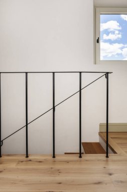 Siyah minimalist metal parmaklıklı, düz beyaz duvarlı ve kare pencereli meşe ağacından basamaklı bir ev.