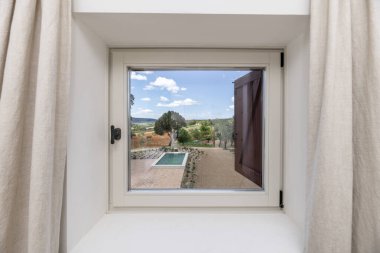 Yüzme havuzlu bir alana bakan kare pencereli bir oda.