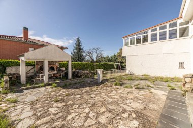 Granit taş zeminli bir arsası olan bir dağ evinin arka cephesi, kuru ağaçlar ve üstü kapalı bir barbekü.
