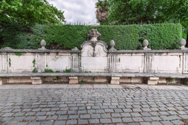 Parkta, üzerinde çit ve taş kaldırım taşı zeminleri olan süslü, antika bir taş bank.