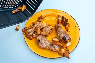 Pişmiş tavuk budu ve patatesleri güzel mavi bir masada tavada tavada çevirmeyi.